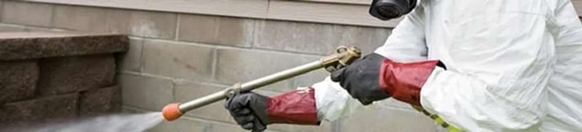 Pest control technician applying exterior insect treatment along a home foundation in Columbus, OH