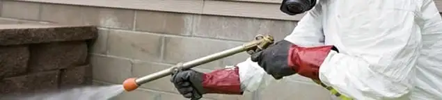 Pest control technician applying exterior insect treatment along a home foundation in Columbus, OH