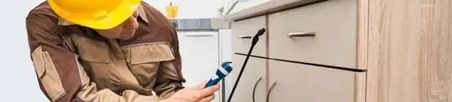 Roach exterminator applying treatment under kitchen cabinets in Columbus, OH