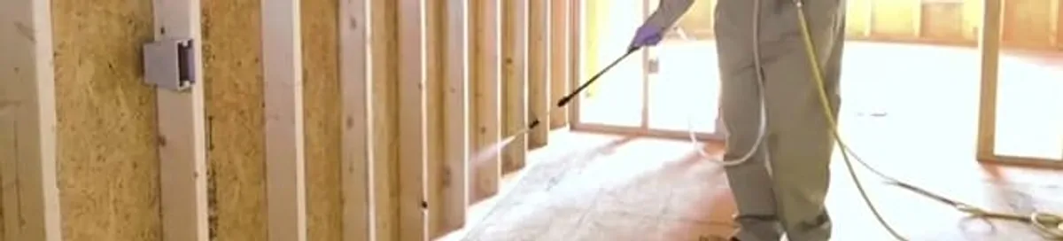Termite treatment technician applying spray along framing and unfinished walls in Columbus, OH